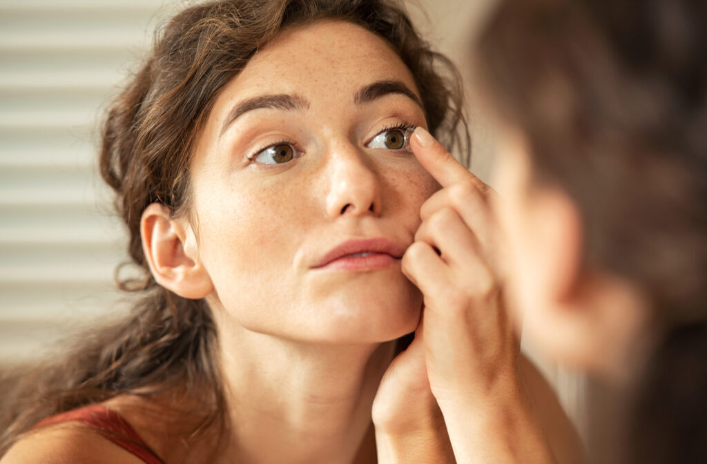 Young woman putting contact lens into her eye